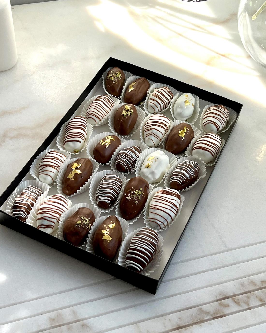 Black gift box of chocolate-dipped dates with drizzle and gold flakes