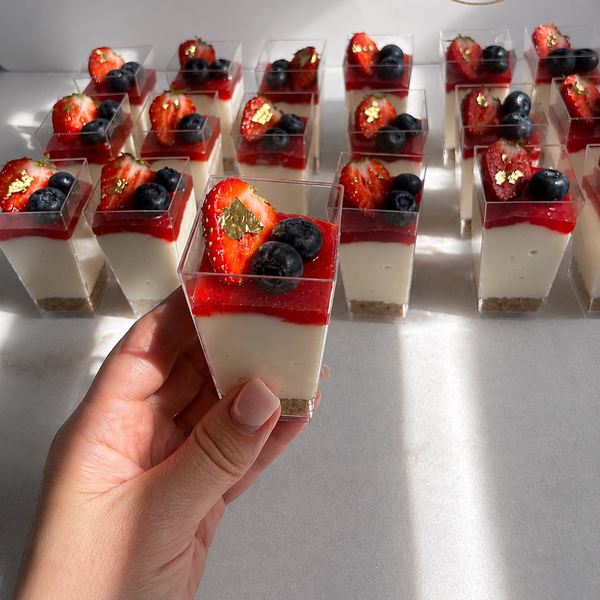 Hand holding a mini cheesecake cup with berries