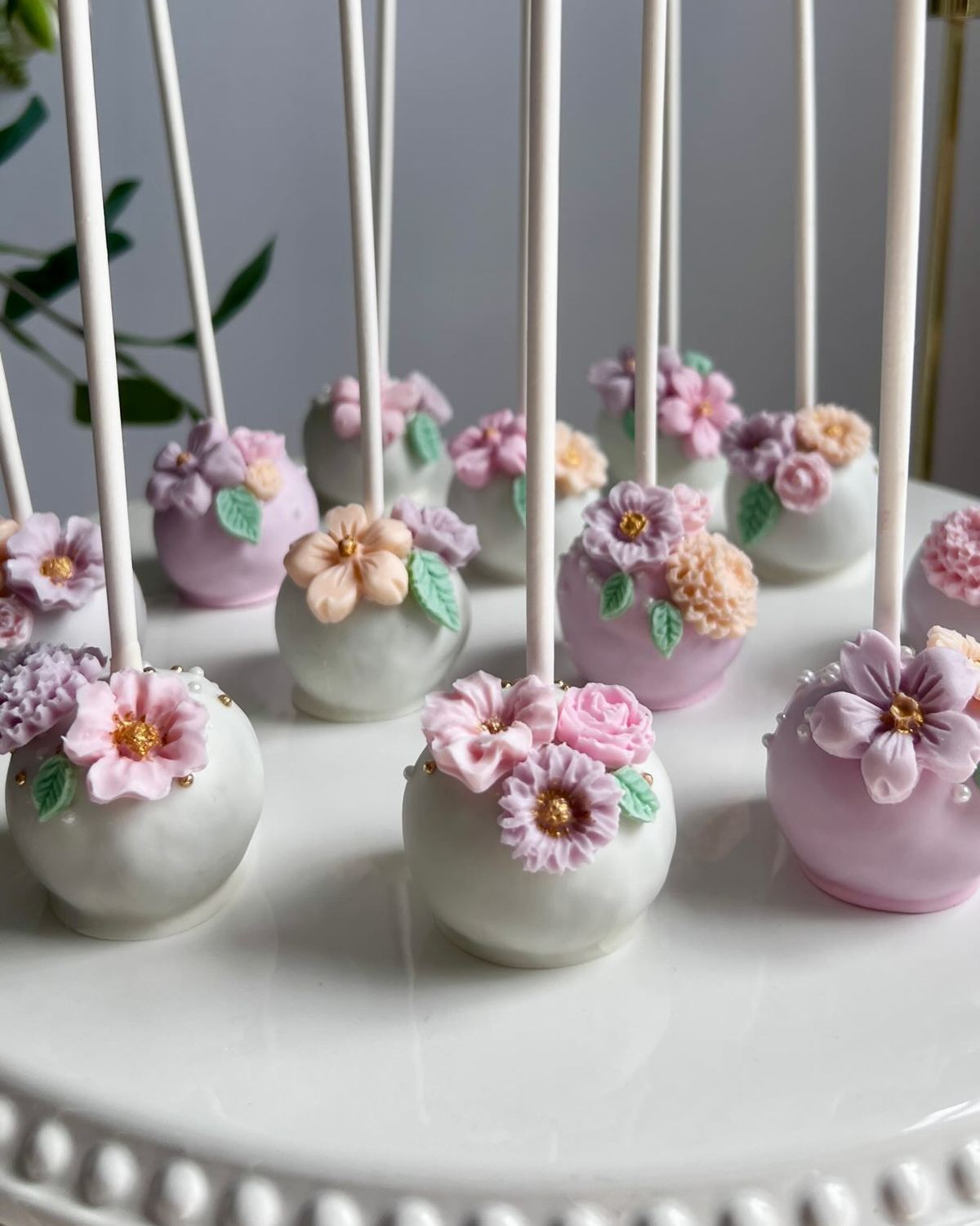 Pastel cake pops decorated with sugar flowers on a white cake stand