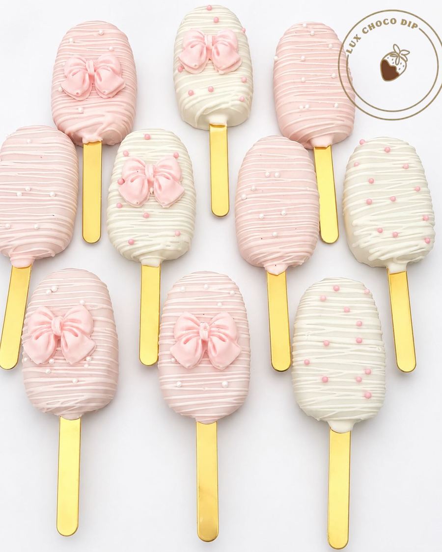 Pink and white cakesicles with sugar bows and gold sticks